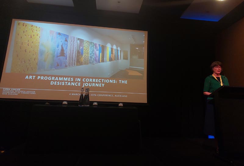 Fiona Conlon stands in front of a large screen with the words "Arts programmes in prisons: the desistance journey”